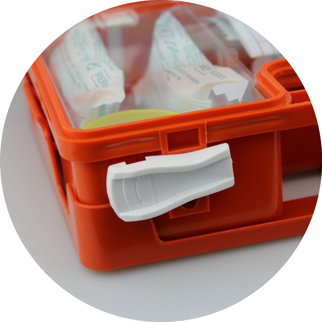 Image d'une trousse de secours orange, fermée avec un clip blanc. La trousse est partiellement transparente, montrant le contenu à l'intérieur, notamment des bandages et d'autres fournitures médicales.  